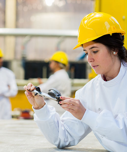 Student wearing a yellow hardhat looking at some measuring equipment.