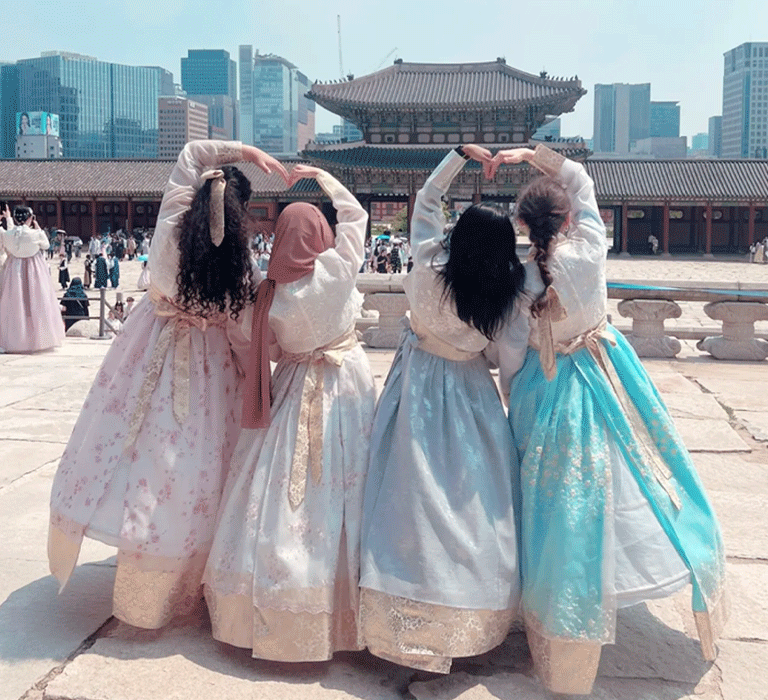 Four students in hanboks in front of a Korean temple.