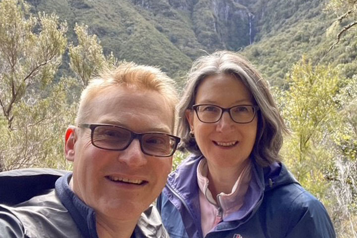 Two people outside smiling at the camera with a set of hills in the background