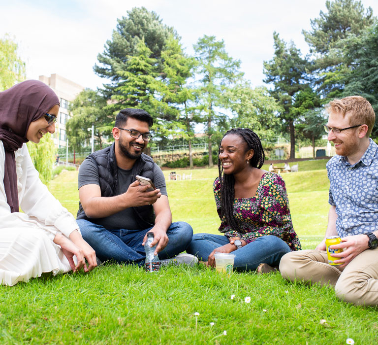 Four students sitting on the grass on Bradford's campus