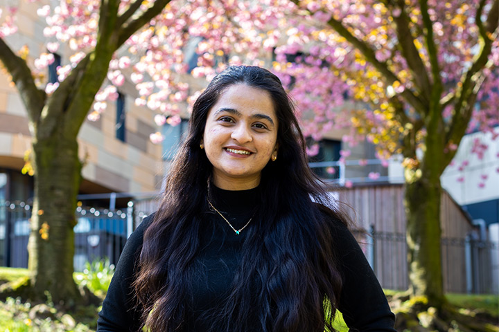 A student smiling at the camera under blossoming trees