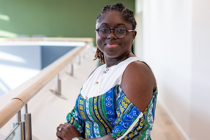 A person leaning on a railing, smiling at the camera in a well-lit indoor space.