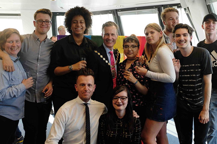 A smartly dressed person surrounded by students all smiling at the camera