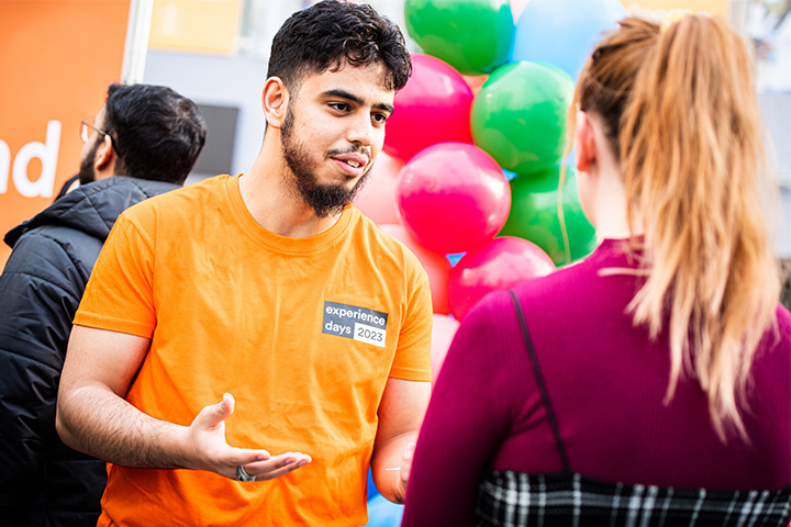 A student representative wearing an orange branded shirt talking to a prospective student