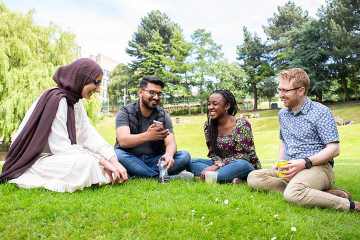 Four students sitting on the grass and laughing.