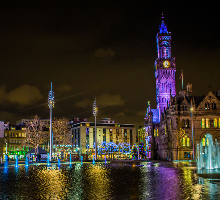 Bradford City Hall and Centenary Square at night with multicoloured lights and fountains