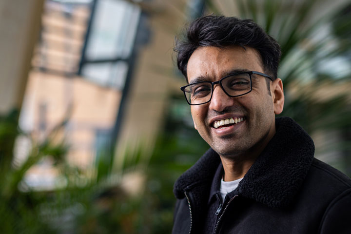 A student smiling at the camera and standing in front of plants