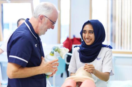 A student smiling whilst being taught CPR by her mentor