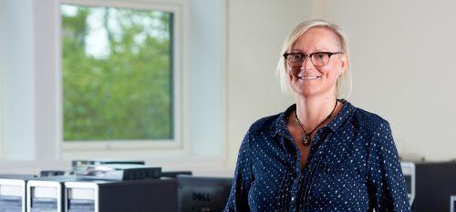 Andrea Cullen, BSc Computing with Management (2000) and PhD Operations and Supply Chain Management (2004) wearing glasses and standing in front of a computer.