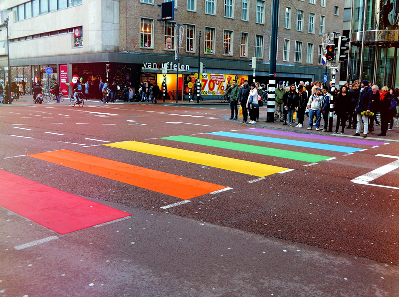 Rainbow coloured zebra crossing with crowd waiting to cross.