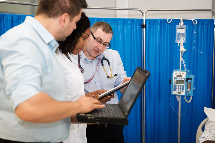 Three medical staff collectively looking at a clipboard and laptop.