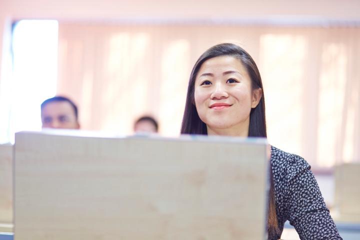 Student smiling sitting behind Bloomberg Trading room monitor