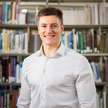 A student standing in front of a shelf of library books.