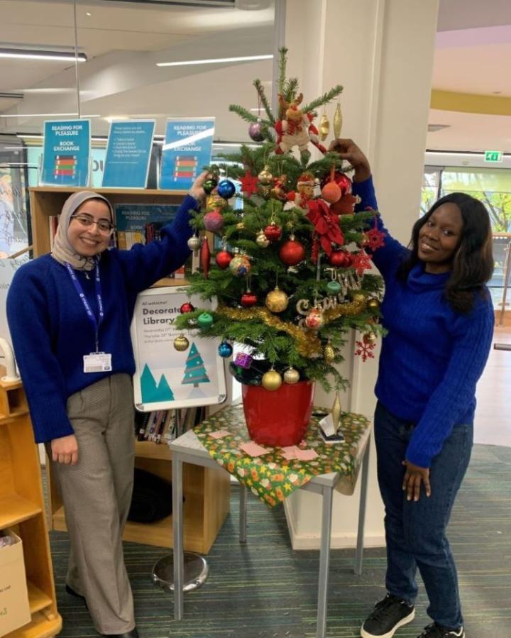 Two Student Event Coordinators decorating the library Christmas tree