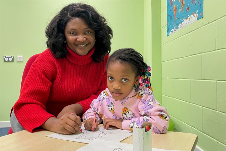 A woman and a girl sitting at a table with colouring books