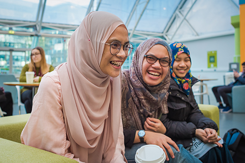 Three students sat together and laughing in the Atrium