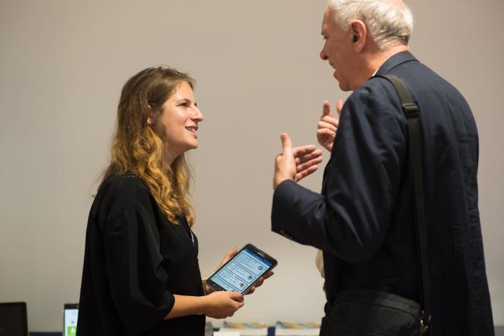 A male University employee is talking with a female student who is holding a tablet device.