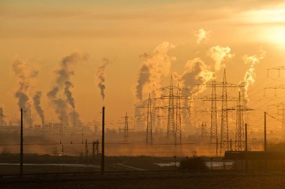 Smoke rising from chimneys set against a hazy orange sunset sky