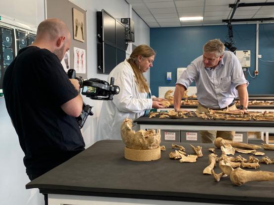 Ray Mears being filmed talking to Jo Buckberry with a skeleton laid on a bench