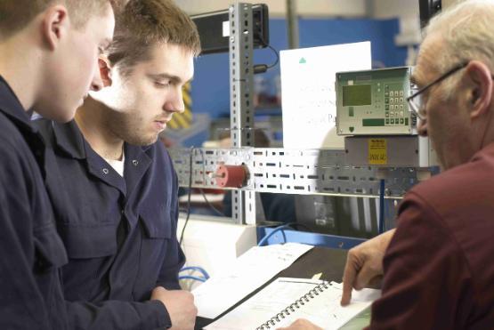 Two people working in a factory are shown a document by a co-worker