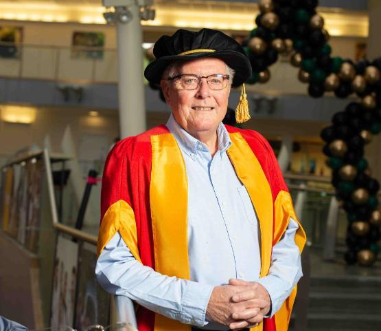 Person in graduation gown stands by barrier in atrium having picture taken