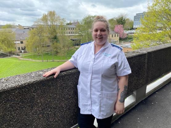 Student dressed in white nursing shirt stands with grass area at university behind