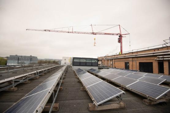 Solar panels on a building's roof in the foreground with a crane above in the background