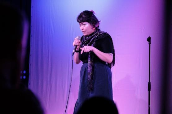 A person stands up in front of a curtain holds a microphone and gives a stand-up comedy show