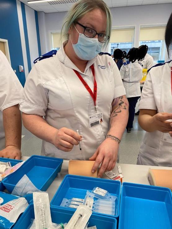 A university student in a nursing uniform wearing a face mask holds a syringe during a practical medical lesson