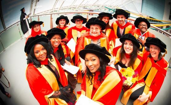 A group of graduates stare into the camera wearing gowns and hats