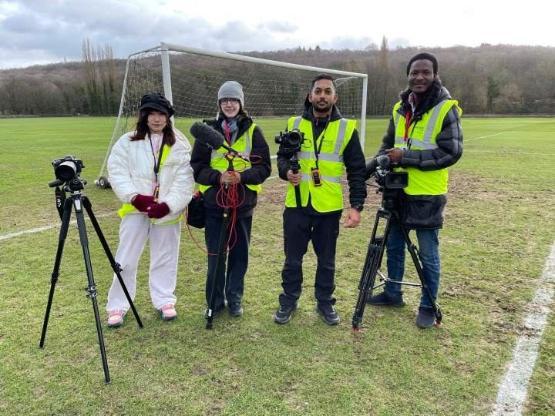 a group of four students in high-vis jackets standing on a grass football pitch