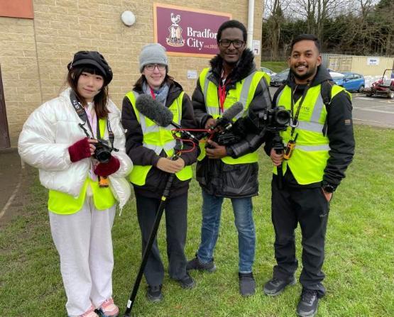 a group of four students wearing high-vis jackets holding video camera equipment