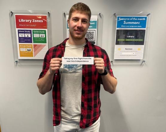 A student stands up holding up small piece of paper in front of them