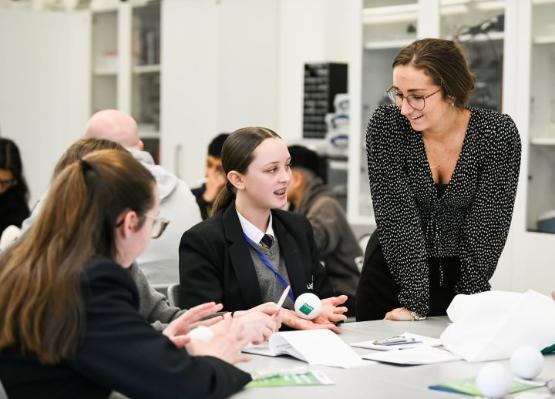 An adult stood up talking to two school students who are sat down