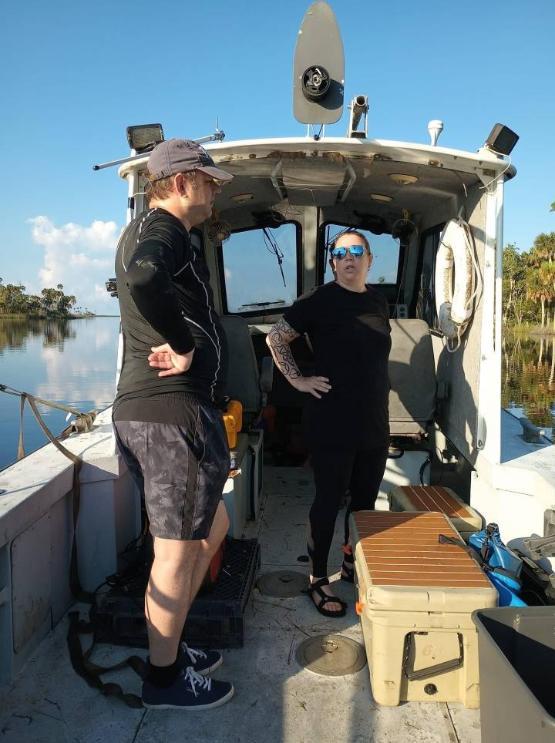 Two university staff stood up on a boat in the USA with a blue sky behind them