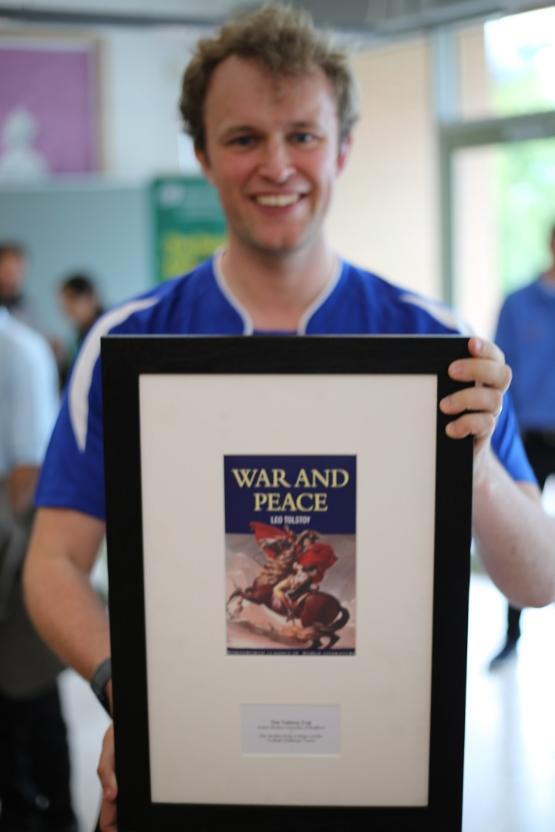 A football player in kit holds a framed trophy in front of them