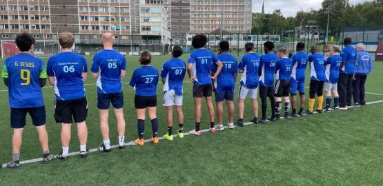 A number of people dressed in football kit line up on the halfway line of the pitch with their backs to the camera for a photograph