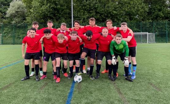 A large group of football players in kit with red shirts line up for a team group photograph on the pitch half standing and half of them crouching in front of them