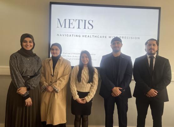 Five students dressed smartly stand up in front of projector screen with Metis written on it