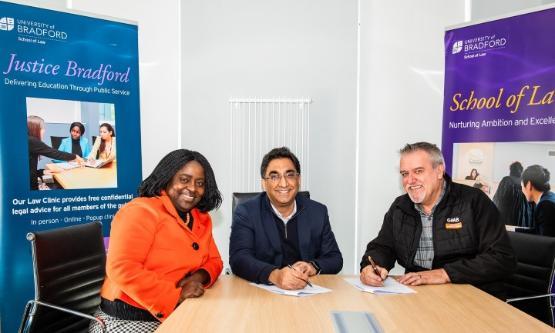 Three people sat behind a wooden desk in a room