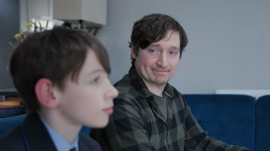 An adult looking over proudly at a young boy as they sit on a sofa together