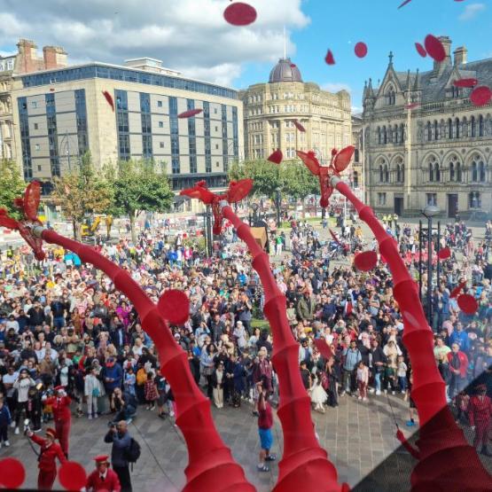 Three tall red giraffe style structures hang over a large crowd of people in a city square area