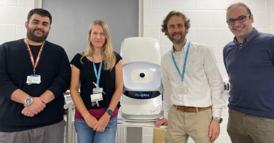 Two university staff members stand either side of a large white machine used for optometry