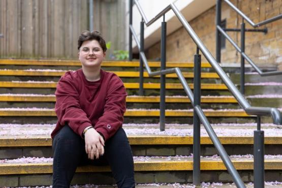 A student sat down outside on some concrete steps with a handrail to their left