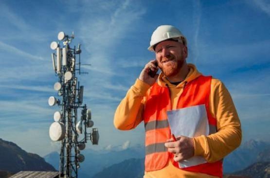 A person in an orange coloured hi vis jacket wearing a hardhat talking on a mobile phone holding a paper