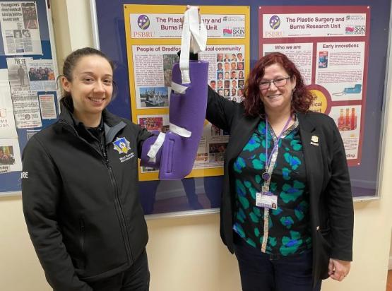 A firefighter wearing a purple coloured arm sling which is being held up by a university staff member