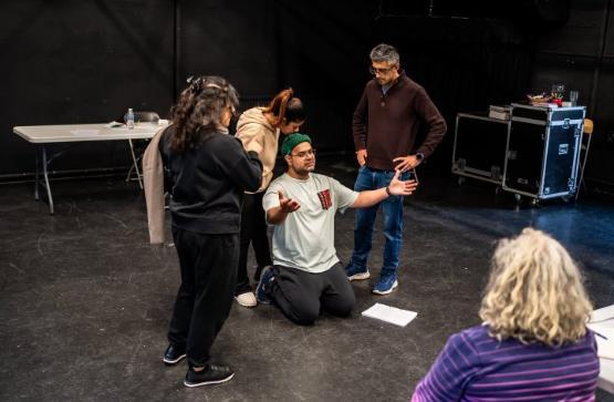 A play rehearsal picture of a person on their knees surrounded by three other people