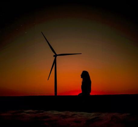 A silhouetted figure kneeling with a wind turbine in the background