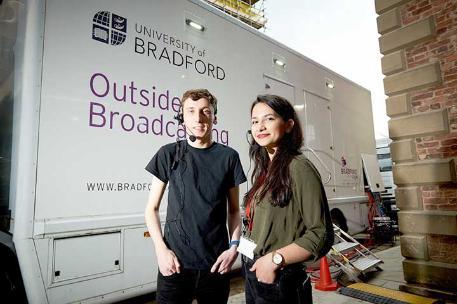 Students wearing talkback headsets standing next to the university outside broadcast truck