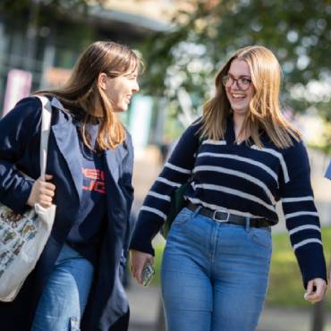 Two students smile and laugh to each other on campus.